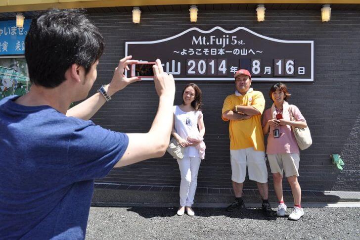 日付入りの富士山五合目の看板前で記念撮影をする参加者