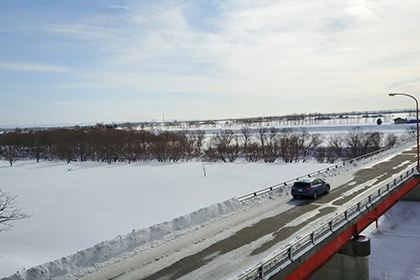 雪が降る石狩川とドライブ中のレンタカー