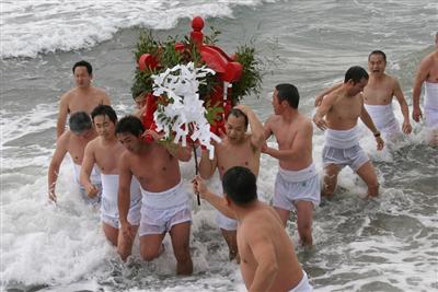 さらしをまいた青壮年たちが波をかぶりながらも海岸沿いを泳ぐ